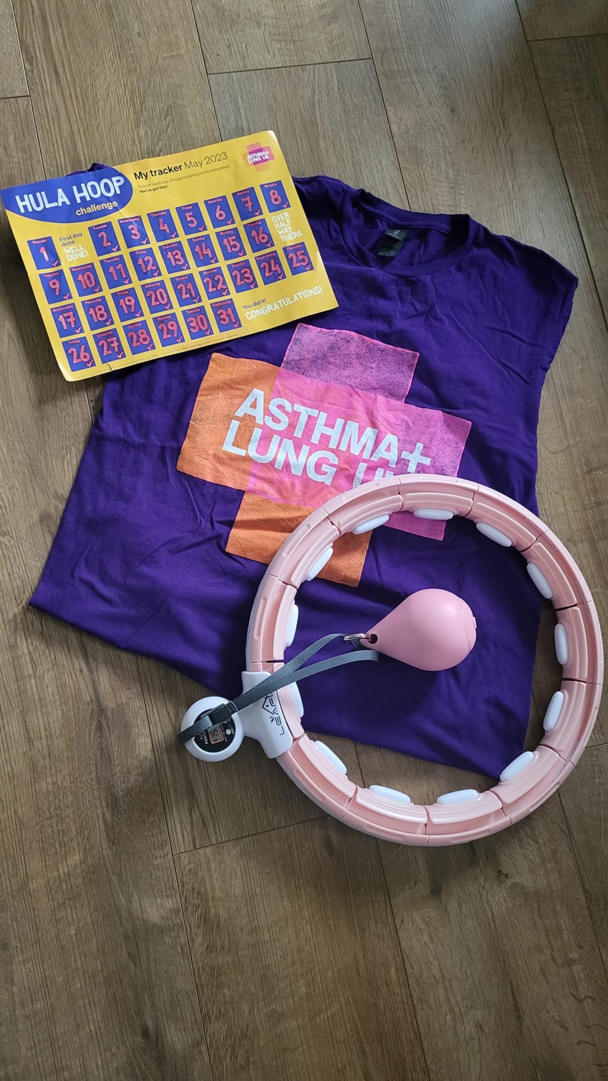 Purple Asthma + Lung UK t-shirt, a hula hoop with a weighted ball, and a May 2023 Hula Hoop Challenge tracker laid out on a wooden floor