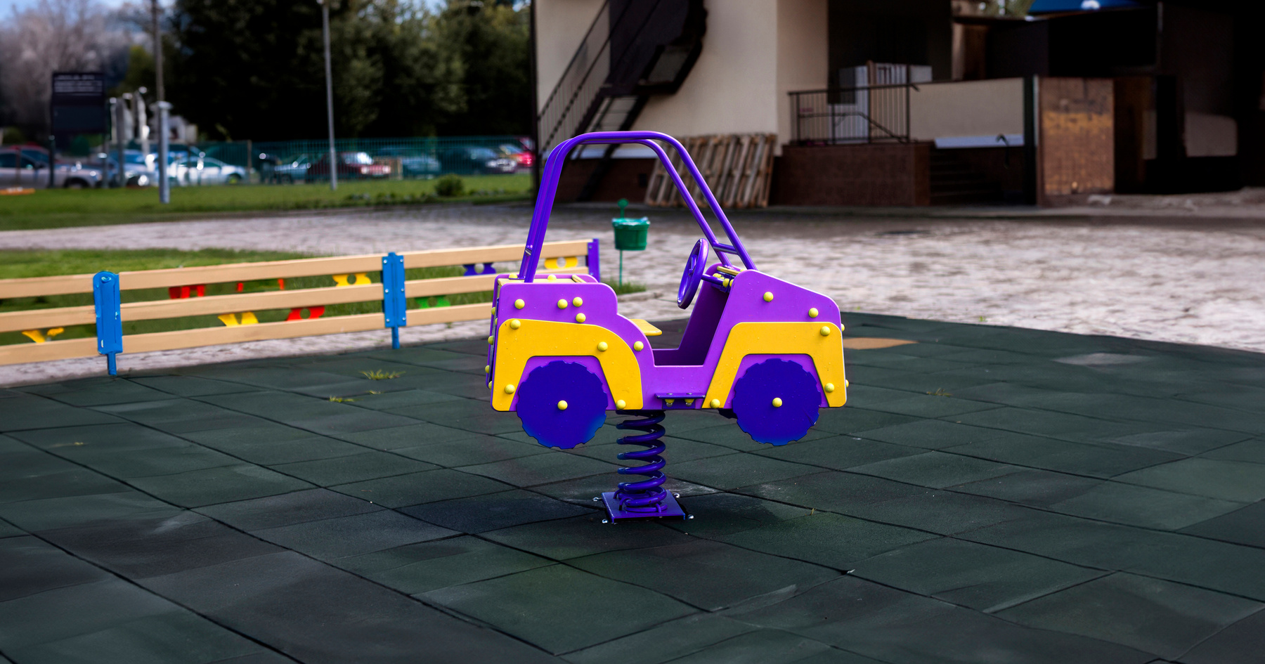 A purple and yellow spring-mounted toy car on a green rubber playground surface