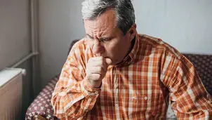 A man in a plaid shirt is coughing into his fist