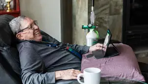 Man with oxygen tank laughing with people on his tablet