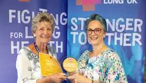 Two smiling women hold an award and a certificate
