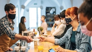 A barista wearing a mask serving coffee