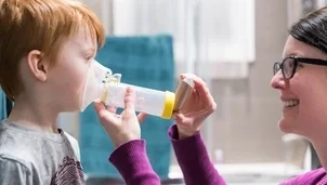 Parent helping their child use an inhaler with a spacer and face mask