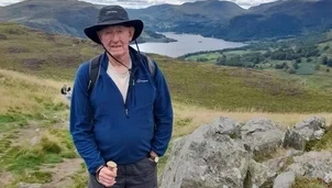 A man with a black hat and a blue fleece is stood on a hill.