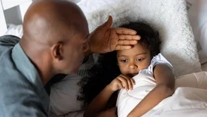 Child lying down and person checking their temperature