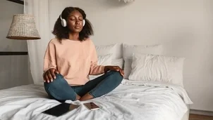 woman sitting on bed in headphones meditating