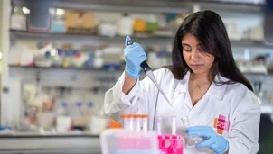 Researcher in a lab coat uses a pipette to transfer liquid into a flask at a laboratory bench