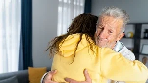 An elderly man with a nasal oxygen tube hugs a woman in a yellow hoodie