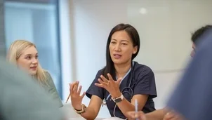 A healthcare professional speaks during a meeting, gesturing with her hands as others listen
