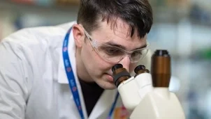 Researcher in safety goggles examines a sample through a microscope in a laboratory