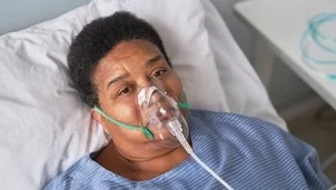 A hospital patient lies in bed wearing an oxygen mask