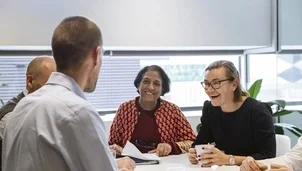 A group of people sit around a table, smiling and talking during a meeting