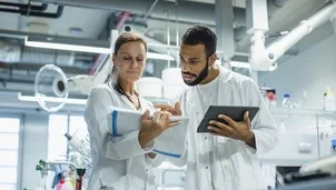 Two scientists in lab coats discuss notes and data in a laboratory
