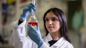 Scientist in lab coat examining a flask with red liquid